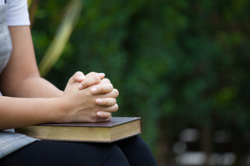 Woman hands folded in prayer on a Holy Bible  for faith concept
